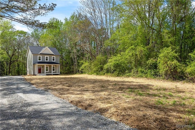 exterior space with a porch, a view of trees, and gravel driveway