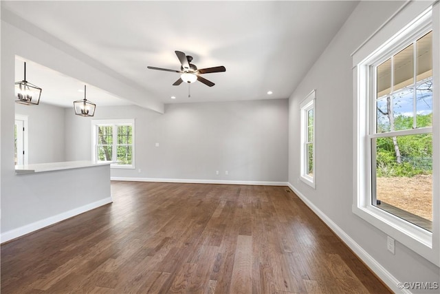 unfurnished living room featuring recessed lighting, dark wood-style flooring, baseboards, and ceiling fan with notable chandelier