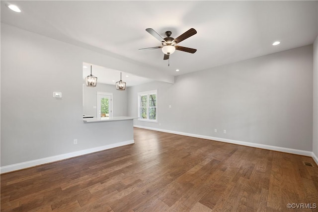 empty room with ceiling fan with notable chandelier, wood finished floors, baseboards, and recessed lighting