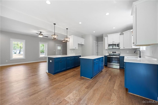 kitchen with blue cabinetry, a kitchen island, stainless steel appliances, a sink, and wood finished floors
