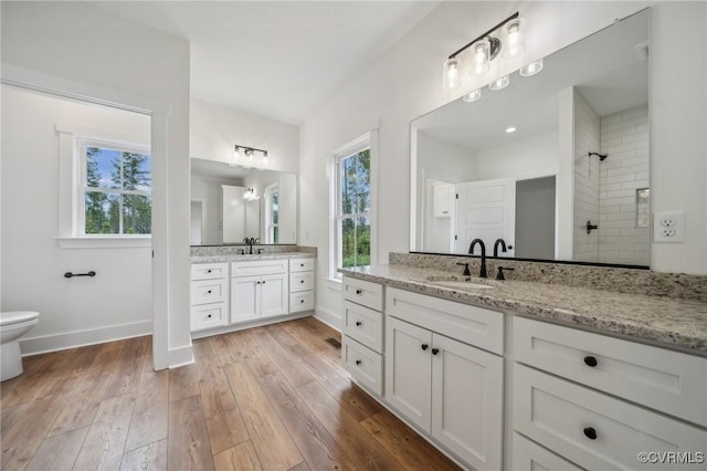 full bathroom with wood-type flooring, a tile shower, baseboards, and a sink