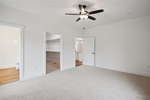 unfurnished bedroom featuring light colored carpet, baseboards, a spacious closet, and ensuite bath