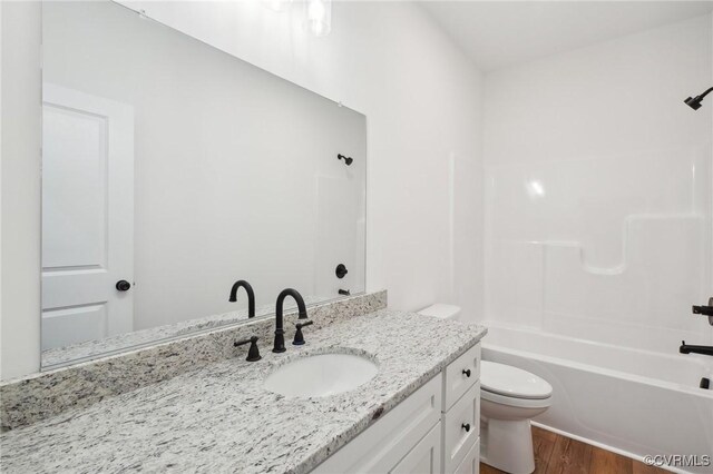 bathroom featuring toilet, wood finished floors, vanity, and shower / washtub combination
