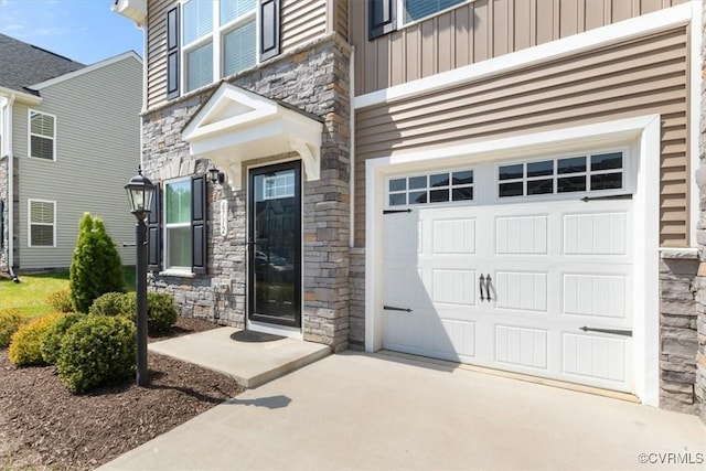 doorway to property with board and batten siding, driveway, stone siding, and a garage