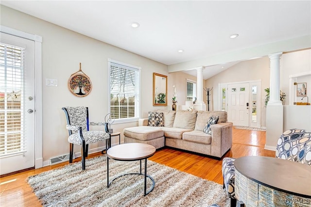 living room with light wood-type flooring, lofted ceiling, a wealth of natural light, and ornate columns
