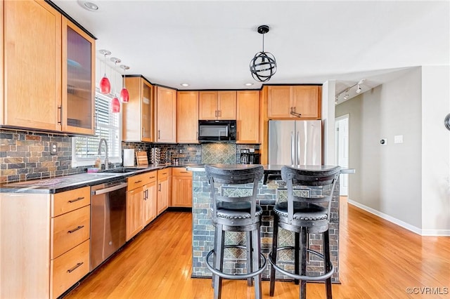 kitchen with stainless steel appliances, light wood-style flooring, a sink, baseboards, and a breakfast bar area