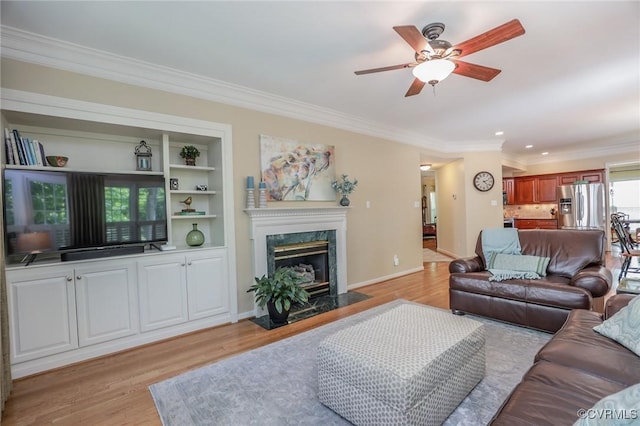 living area featuring ceiling fan, a fireplace, baseboards, light wood-type flooring, and ornamental molding