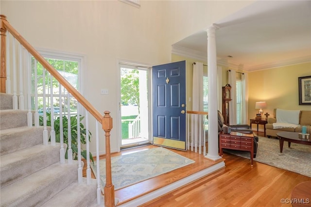 foyer entrance featuring ornate columns, ornamental molding, wood finished floors, and stairway