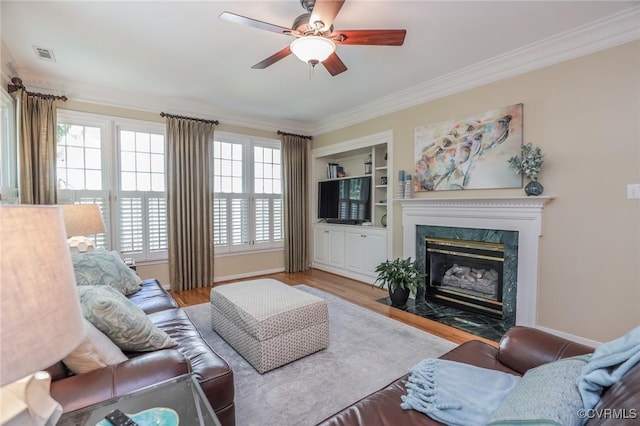 living room featuring crown molding, a premium fireplace, wood finished floors, and visible vents
