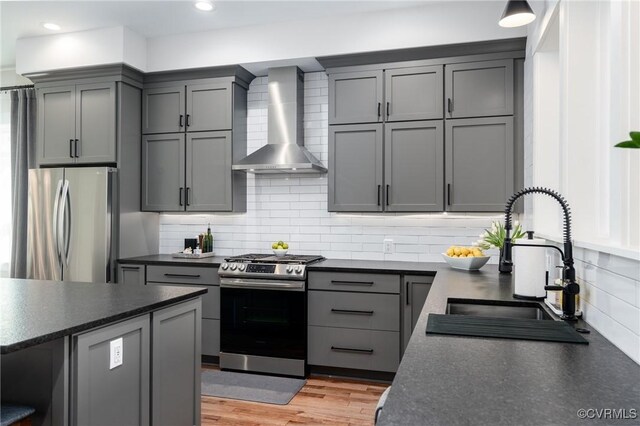 kitchen featuring appliances with stainless steel finishes, wall chimney range hood, a sink, dark countertops, and gray cabinets