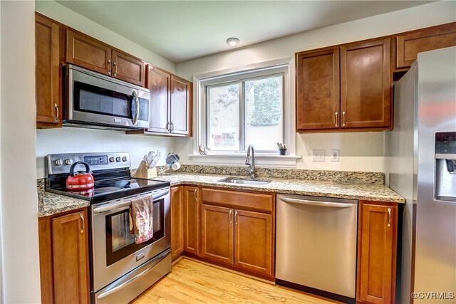 kitchen featuring brown cabinets, light wood-type flooring, a sink, light stone counters, and stainless steel appliances