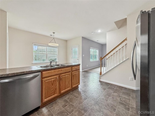 kitchen featuring a sink, dark countertops, baseboards, stone finish floor, and appliances with stainless steel finishes