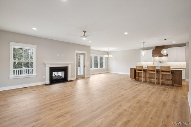 unfurnished living room with baseboards, a multi sided fireplace, light wood finished floors, and recessed lighting
