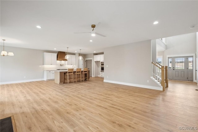 unfurnished living room with recessed lighting, light wood-style floors, stairs, and baseboards
