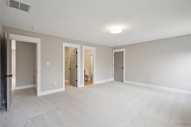 unfurnished bedroom with a walk in closet, ensuite bath, light carpet, baseboards, and visible vents