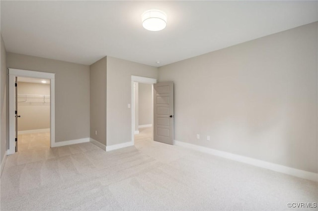 unfurnished bedroom featuring light colored carpet, baseboards, a walk in closet, and a closet