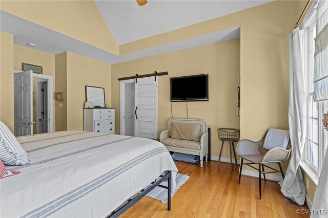 bedroom with baseboards, a barn door, wood finished floors, and lofted ceiling