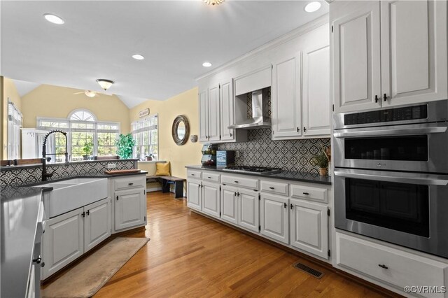 kitchen with wall chimney range hood, a sink, stainless steel appliances, decorative backsplash, and lofted ceiling