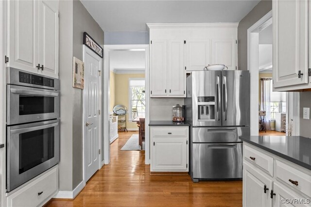 kitchen with dark countertops, stainless steel appliances, white cabinetry, baseboards, and light wood-type flooring