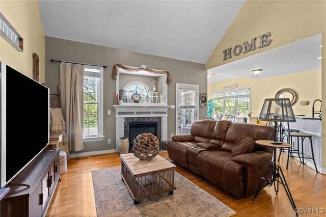 living area with baseboards, a high end fireplace, and light wood-style floors