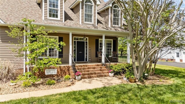 property entrance with a lawn, a shingled roof, and covered porch