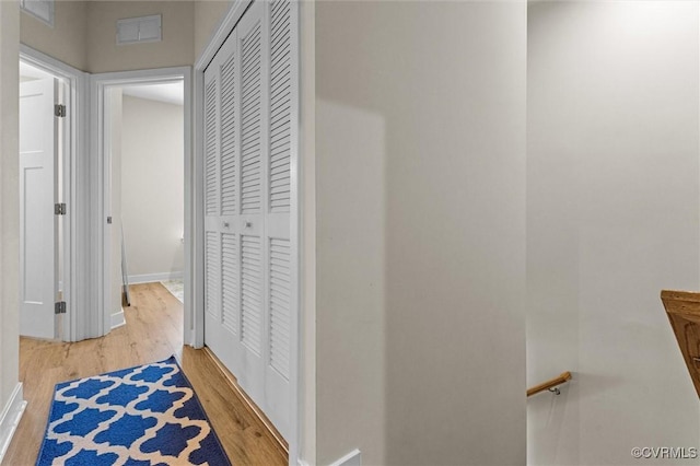 hallway featuring baseboards, light wood-style floors, and visible vents