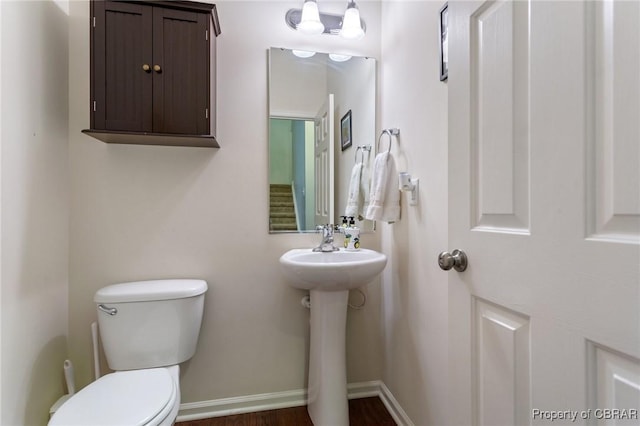 half bathroom featuring wood finished floors, toilet, baseboards, and a sink