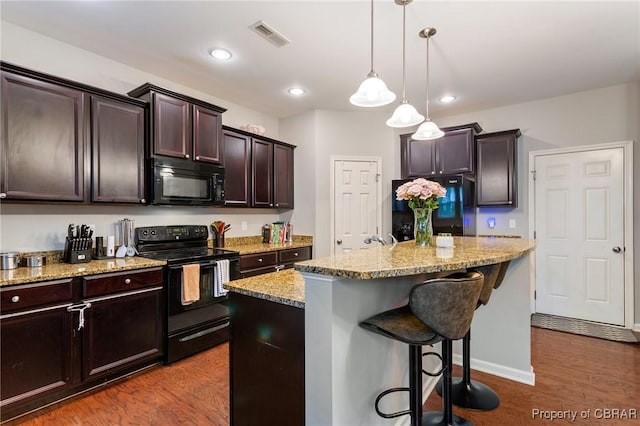 kitchen featuring a kitchen breakfast bar, dark wood-type flooring, light stone countertops, dark brown cabinetry, and black appliances