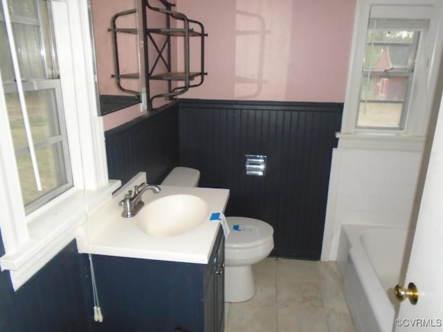 bathroom with tile patterned floors, a wainscoted wall, toilet, a tub to relax in, and vanity
