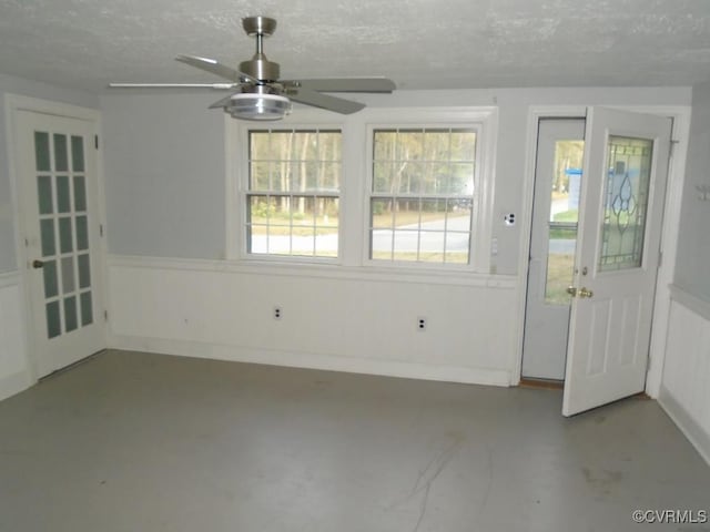 interior space featuring ceiling fan, a wainscoted wall, a textured ceiling, and finished concrete flooring