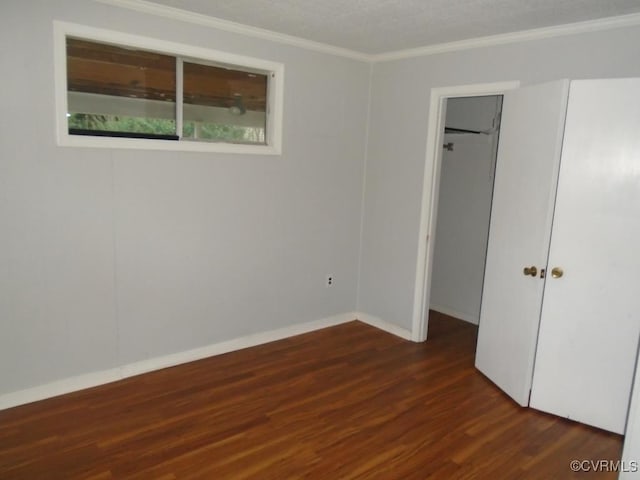 unfurnished bedroom featuring baseboards, wood finished floors, a closet, crown molding, and a walk in closet