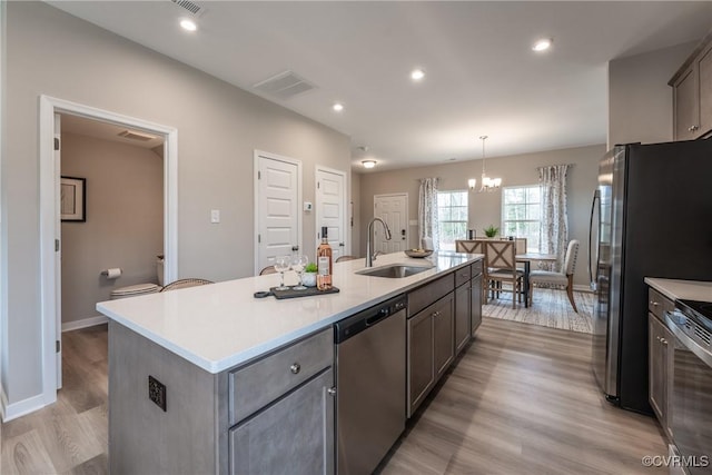 kitchen with appliances with stainless steel finishes, a sink, an island with sink, light wood-type flooring, and visible vents