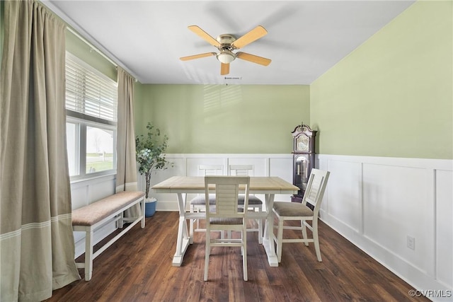 dining space featuring a ceiling fan, a wainscoted wall, a decorative wall, and dark wood-type flooring