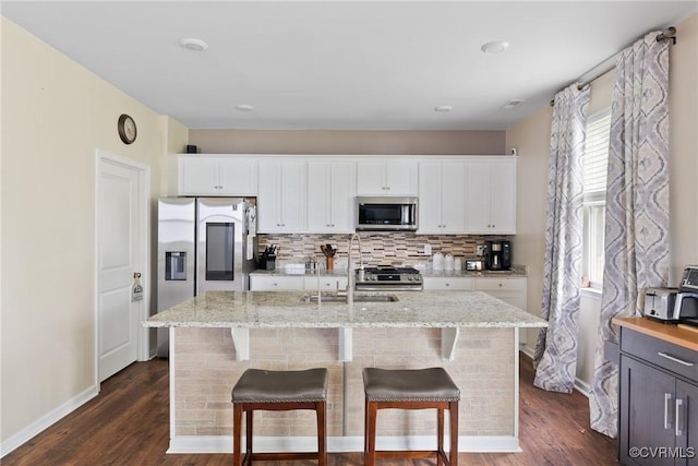kitchen with appliances with stainless steel finishes, a sink, decorative backsplash, dark wood-type flooring, and light stone counters