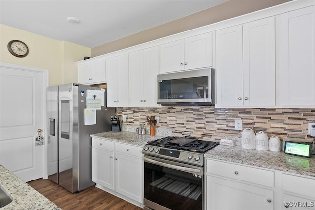 kitchen with appliances with stainless steel finishes, white cabinetry, dark wood-style flooring, backsplash, and light stone counters