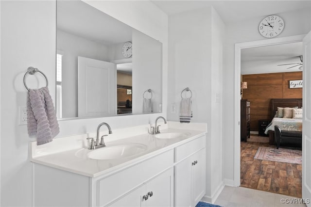 full bath with double vanity, ceiling fan, ensuite bath, and baseboards