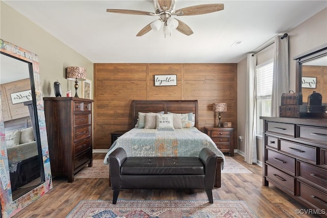 bedroom with wood finished floors, a ceiling fan, and wood walls
