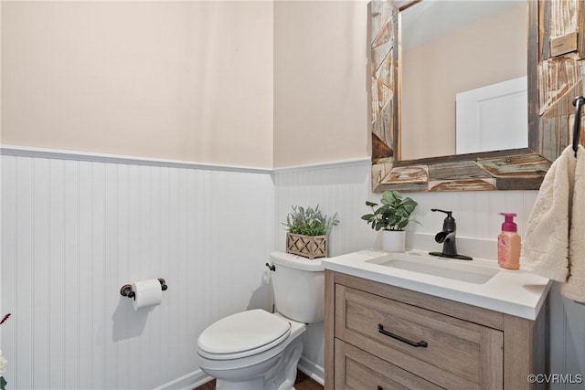 bathroom with toilet, a wainscoted wall, and vanity