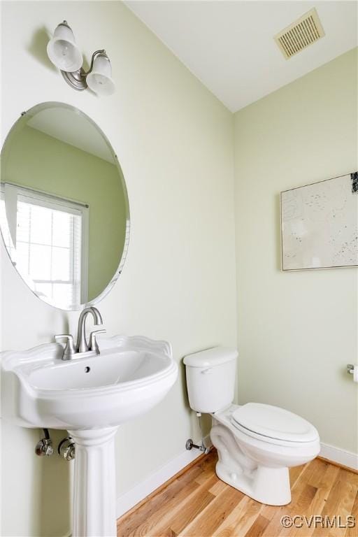 half bath featuring baseboards, wood finished floors, visible vents, and toilet
