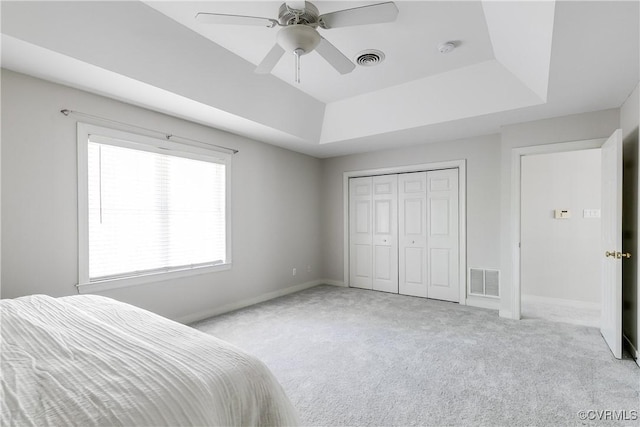 bedroom featuring light colored carpet, baseboards, a tray ceiling, and visible vents