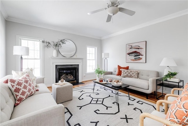 living room with a fireplace with flush hearth, wood finished floors, crown molding, baseboards, and ceiling fan
