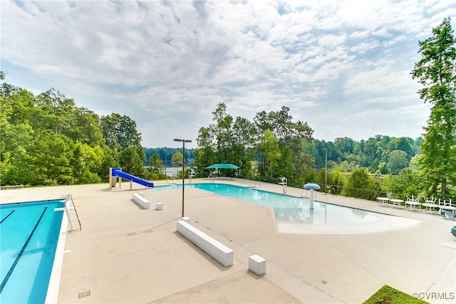 community pool featuring fence, a water slide, and a patio