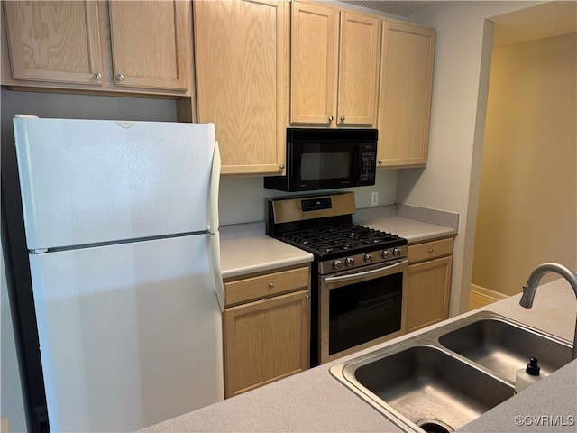 kitchen featuring light countertops, a sink, freestanding refrigerator, black microwave, and gas range