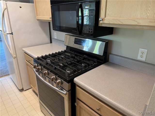 kitchen with freestanding refrigerator, gas range, black microwave, light countertops, and light tile patterned floors