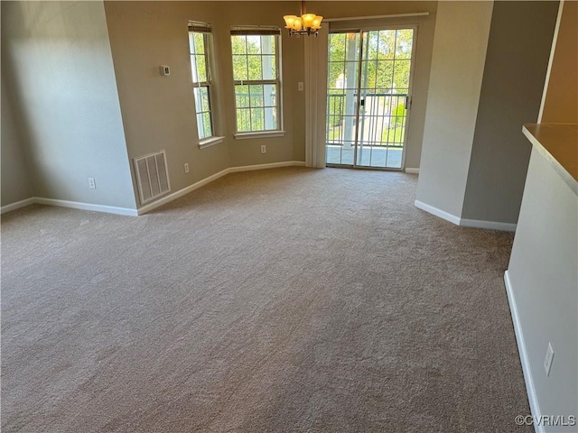 spare room with carpet floors, visible vents, baseboards, and a notable chandelier