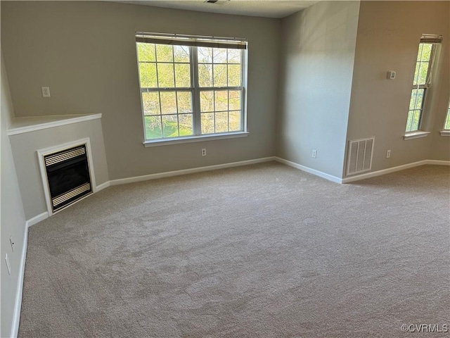 unfurnished living room featuring baseboards, visible vents, a glass covered fireplace, and carpet