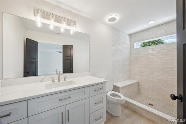 bathroom with a tile shower, wood finished floors, toilet, and vanity