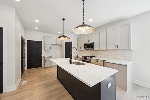 kitchen with a sink, an island with sink, stainless steel appliances, backsplash, and recessed lighting