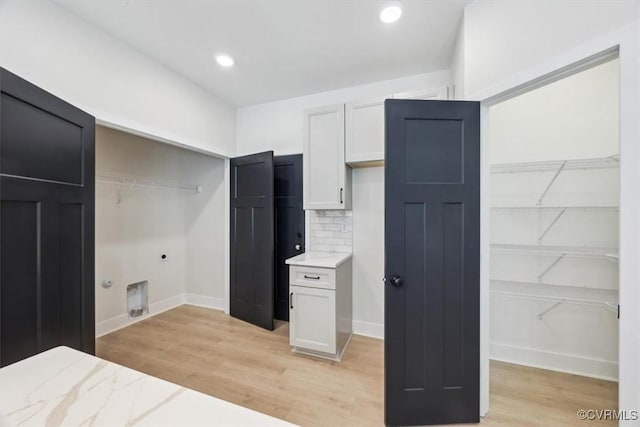 interior space with light stone countertops, light wood-style floors, white cabinetry, and tasteful backsplash