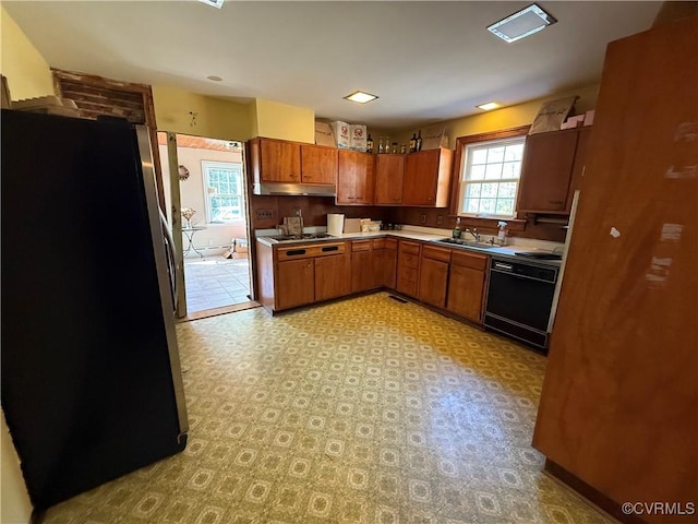 kitchen featuring a sink, brown cabinetry, appliances with stainless steel finishes, light countertops, and under cabinet range hood